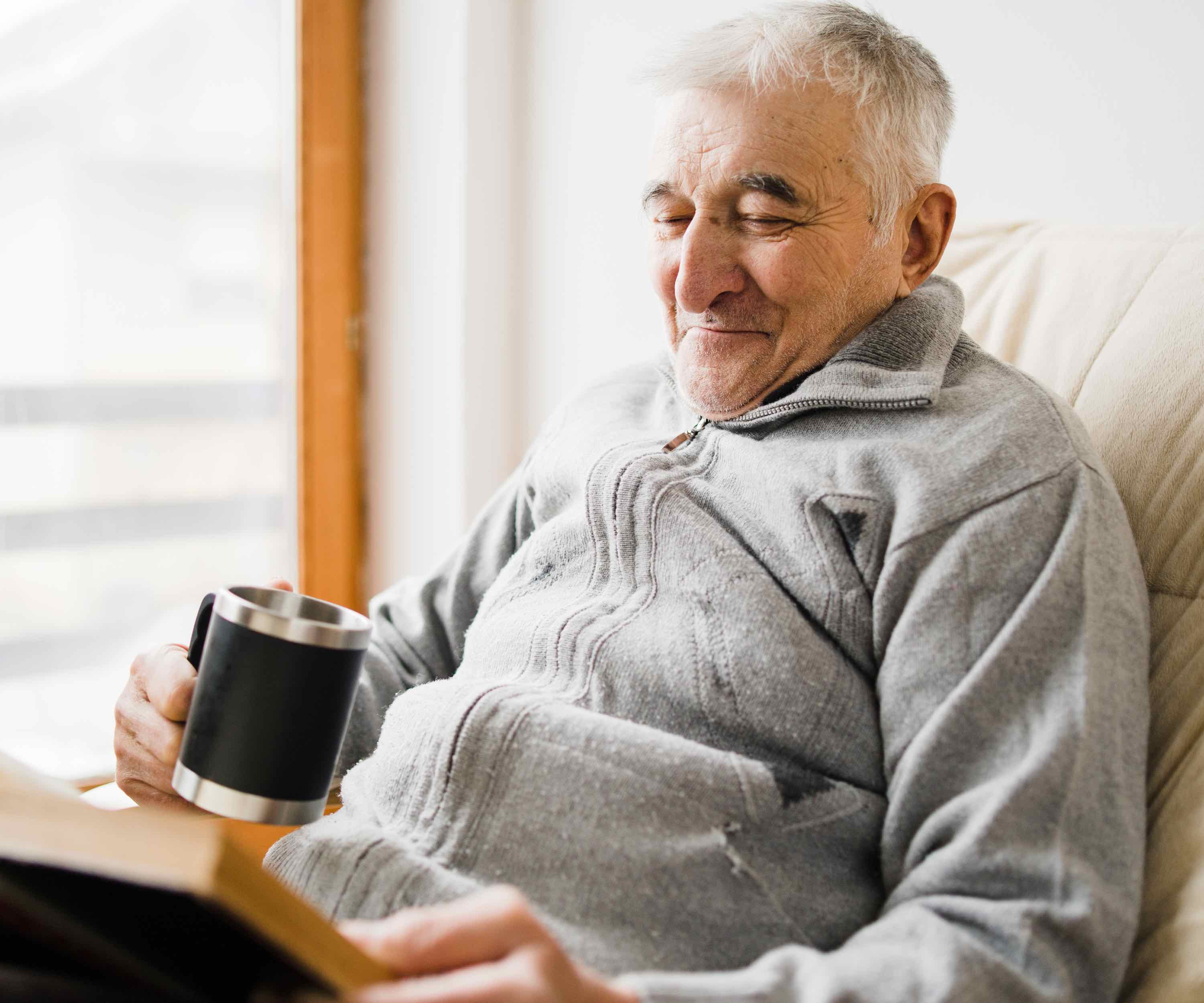 An assisted living resident enjoying a book and a cup of coffee.